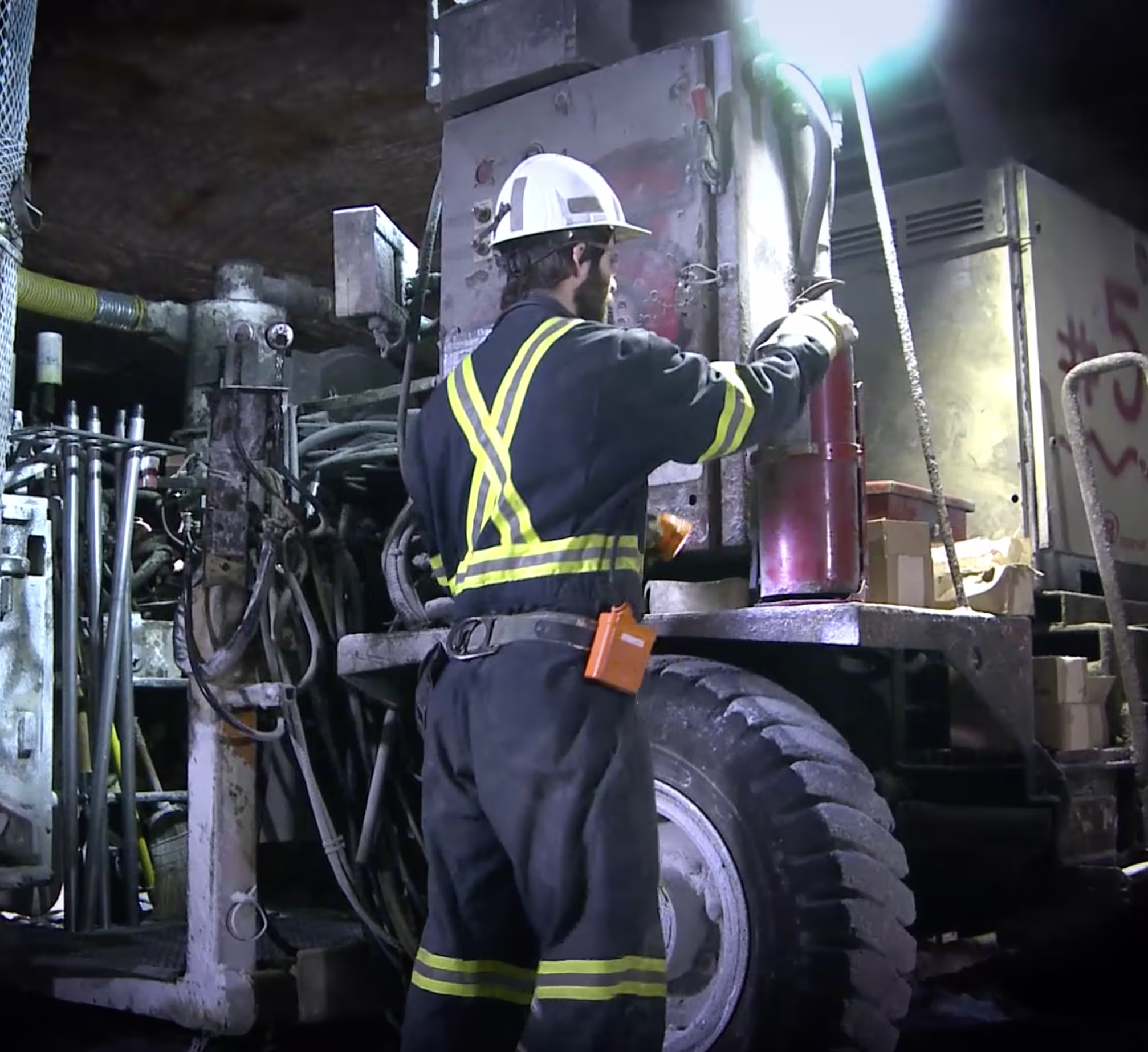 Industrial worker in reflective safety gear operating heavy machinery inside a factory.