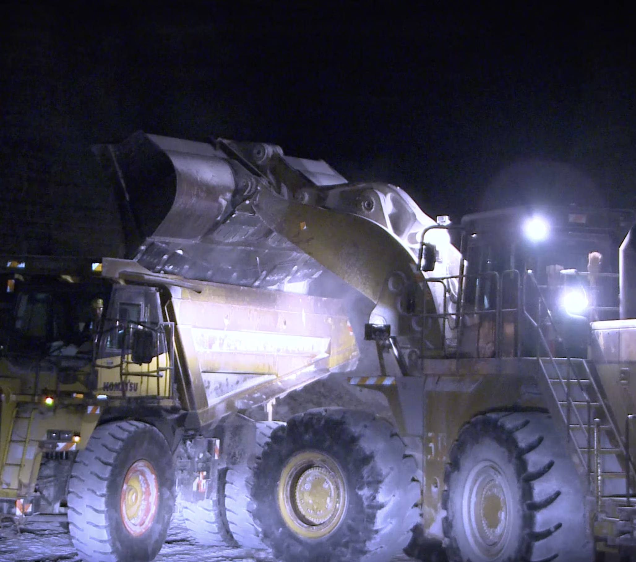 Large construction vehicle operating at night under bright industrial lights at a work site.